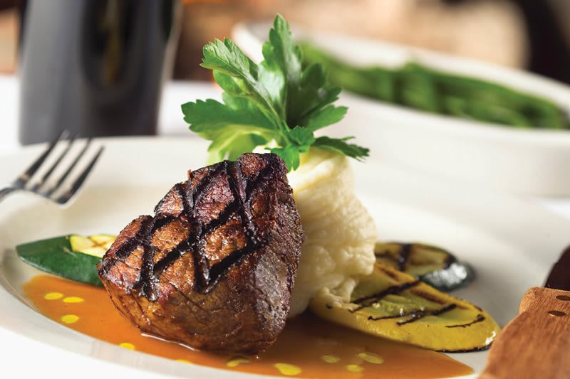 A gourmet dish featuring grilled steak with mashed potatoes and garnished with herbs.