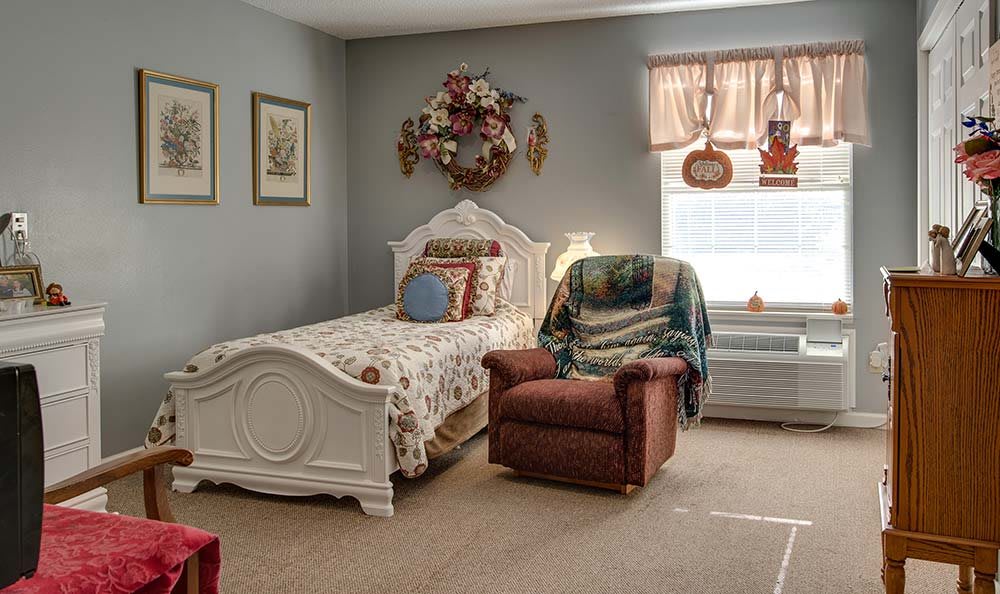 A cozy bedroom featuring a single bed with floral bedding, a comfortable armchair, and decorative wall art.