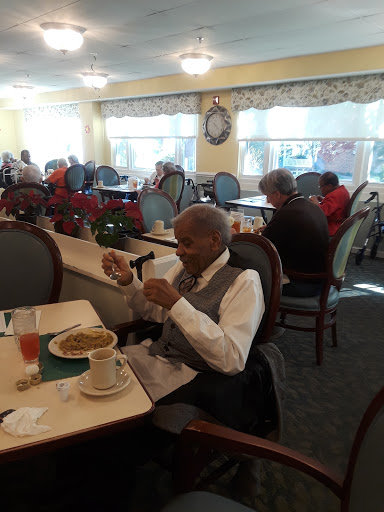 An elderly man enjoying a meal in a cozy dining area with others around.