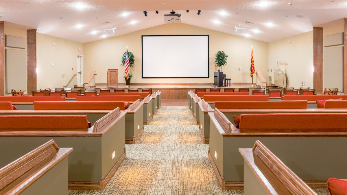 An empty auditorium with rows of seating facing a large screen and podium.