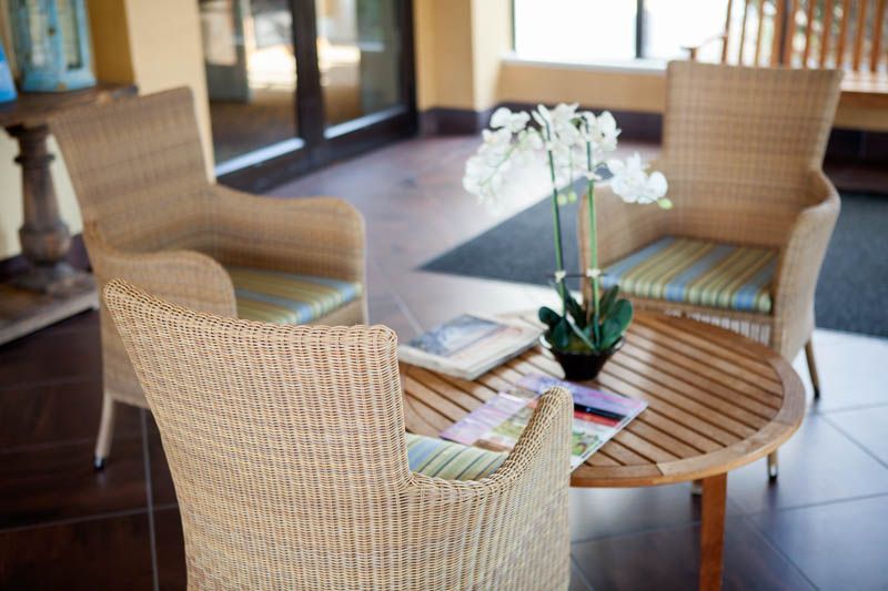 A cozy waiting area with wicker chairs, a wooden table, and a potted orchid as a centerpiece.