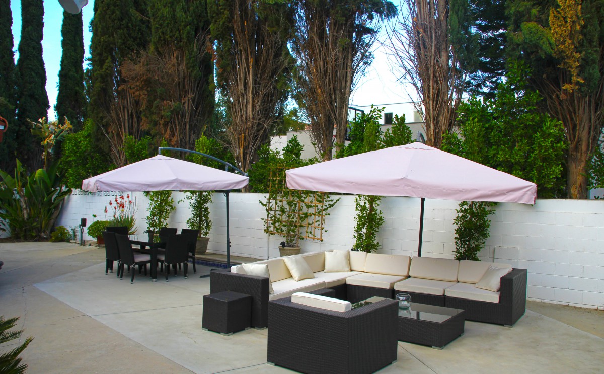 A stylish outdoor patio featuring comfortable seating with umbrellas set against a backdrop of tall trees.