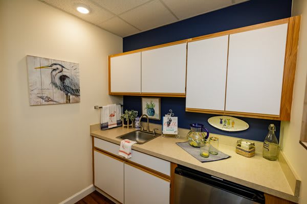 A small kitchen setup with white cabinets, a blue accent wall, and countertop items including a beverage pitcher and cups.