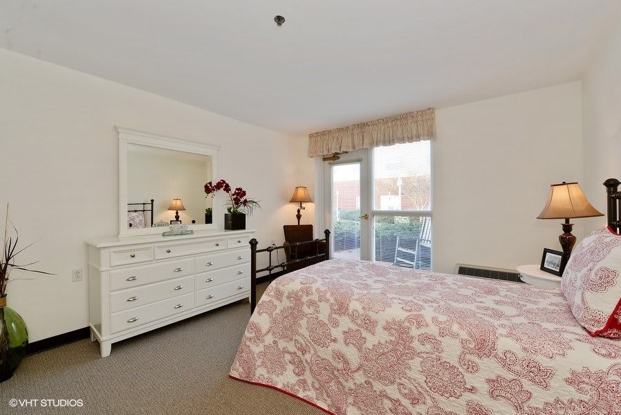 A cozy bedroom with a floral-patterned bedspread, dresser, and window view.