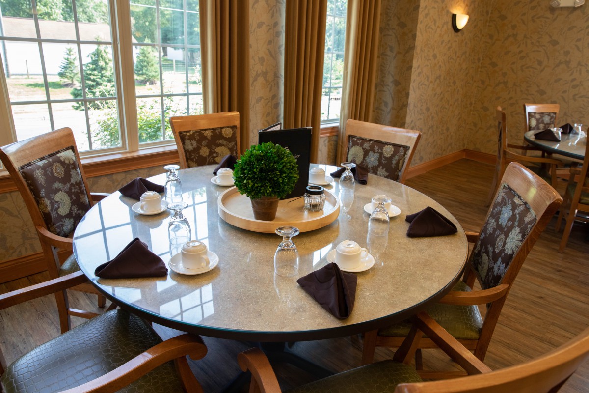 An elegantly set round dining table with napkins and glasses in a well-lit room.