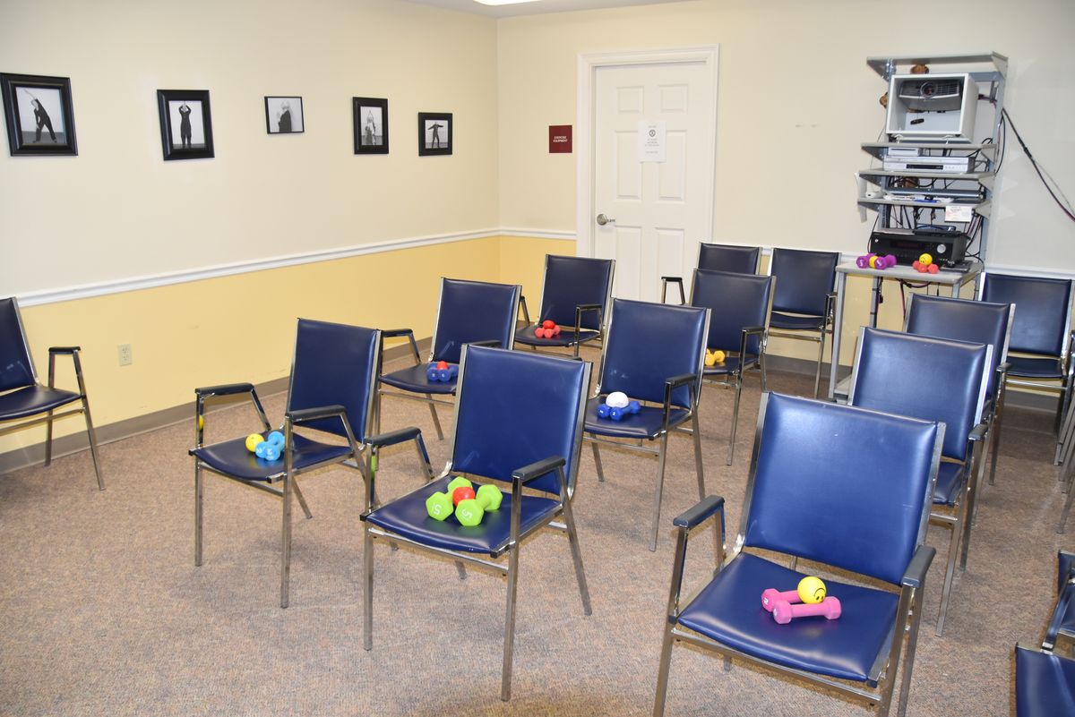 An indoor waiting room setup featuring blue chairs, each holding small exercise equipment like dumbbells and balls.