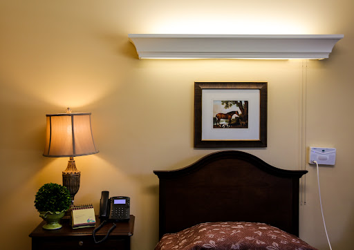A cozy bedroom corner featuring a bedside lamp, wall art, and soft lighting.