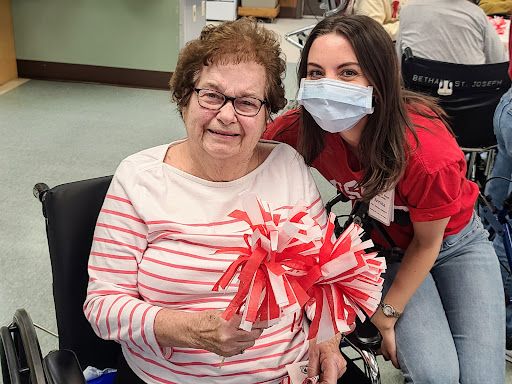 A joyous moment shared between a caregiver and an elderly woman, celebrating with colorful pom-poms.