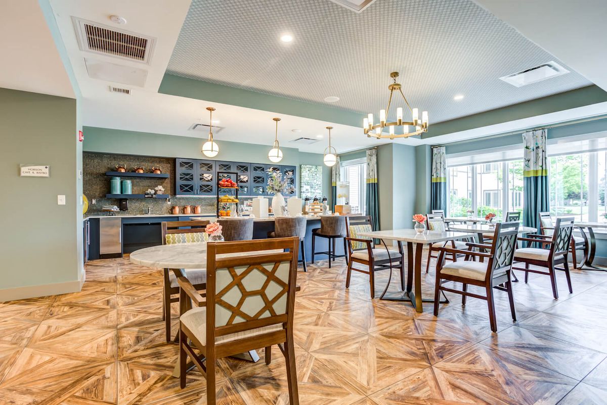 A modern dining area with wooden floors, tables, chairs, and elegant chandeliers.