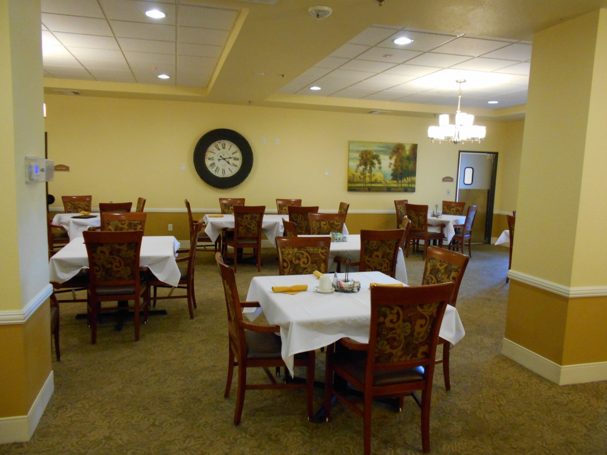 A cozy dining room with neatly arranged tables and chairs, adorned with a large wall clock and artwork.