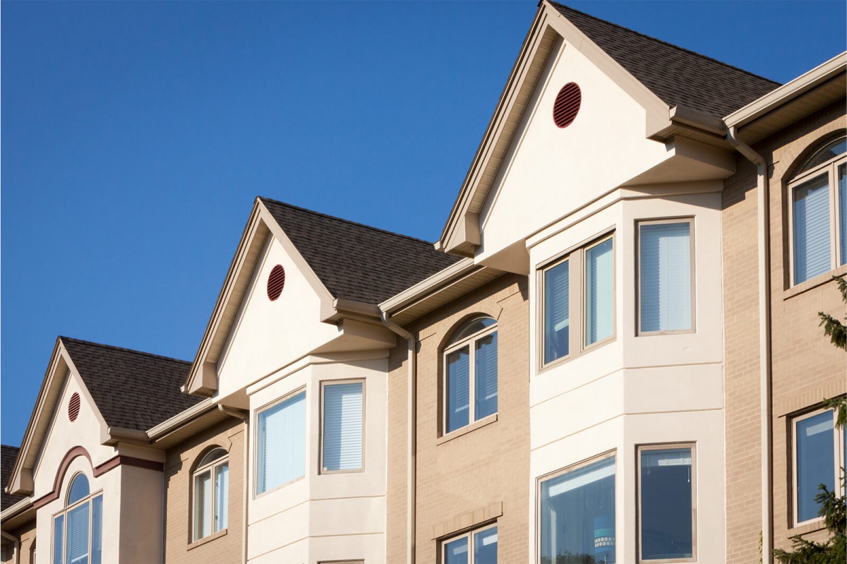 A modern residential building with multiple windows and a gabled roof against a clear blue sky.