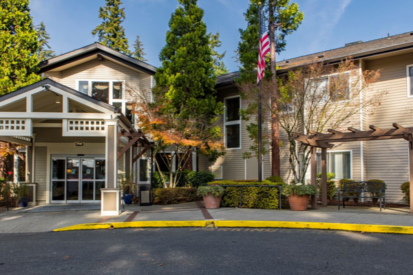 A building with an entrance surrounded by trees and landscaping, featuring a flag flying in the front on a sunny day.
