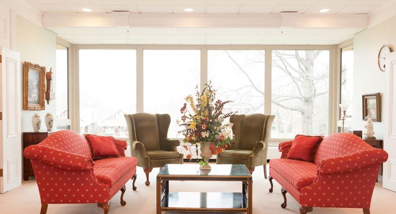 A cozy living room with comfortable seating arrangements, featuring two sofas and armchairs around a glass coffee table with a floral centerpiece.
