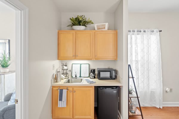 A compact kitchenette with wooden cabinets, a countertop with a microwave and mini fridge, and a small sink for efficient space use.
