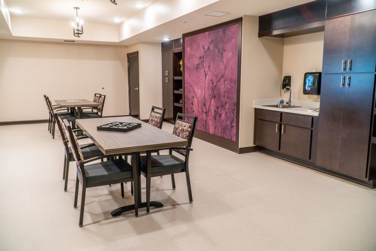 A modern dining area with tables and chairs, featuring a kitchenette and colorful wall art.