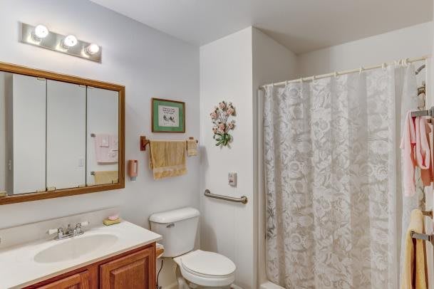 A clean and organized bathroom with a toilet, sink, mirror, and shower area.