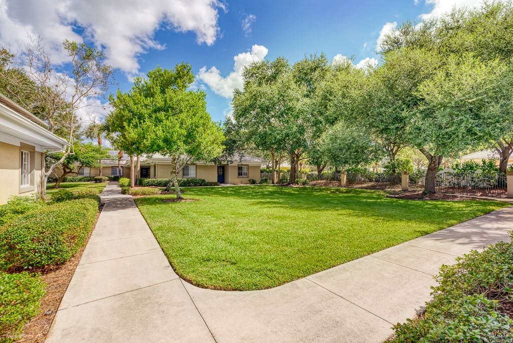 A beautifully maintained garden with lush green lawns and a concrete pathway surrounded by trees under a partly cloudy sky.