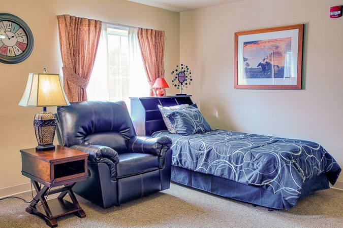 A cozy bedroom with a single bed and an armchair next to a window with curtains.