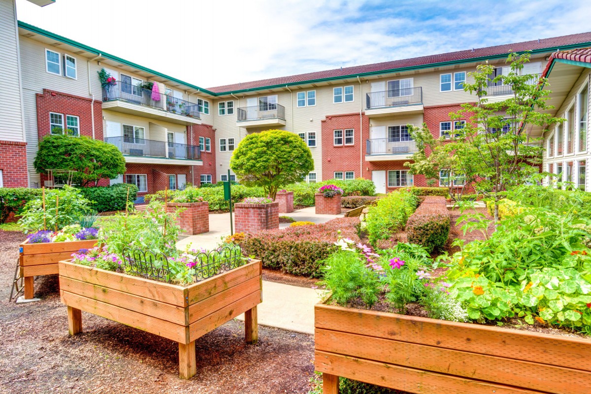 A residential apartment building with a beautifully landscaped garden featuring raised plant beds.