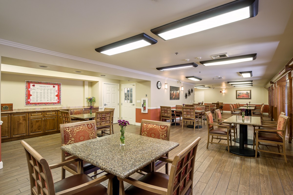 An indoor dining area with wooden tables and chairs, well-lit with overhead lighting.