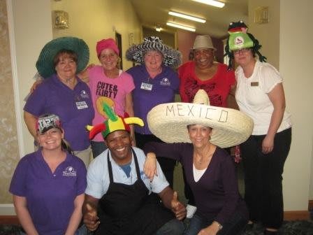 A group of people wearing colorful hats pose together indoors, smiling and enjoying an event.