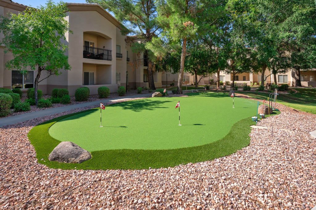 A landscaped apartment courtyard with a putting green surrounded by rocks and trees on a sunny day.