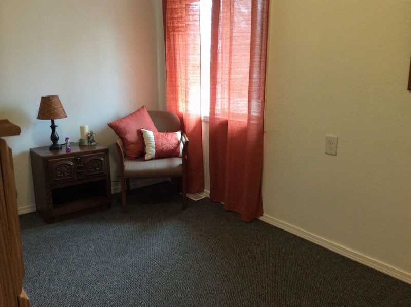 A cozy room with a chair next to a window dressed in red curtains, complemented by a small lamp on an end table.