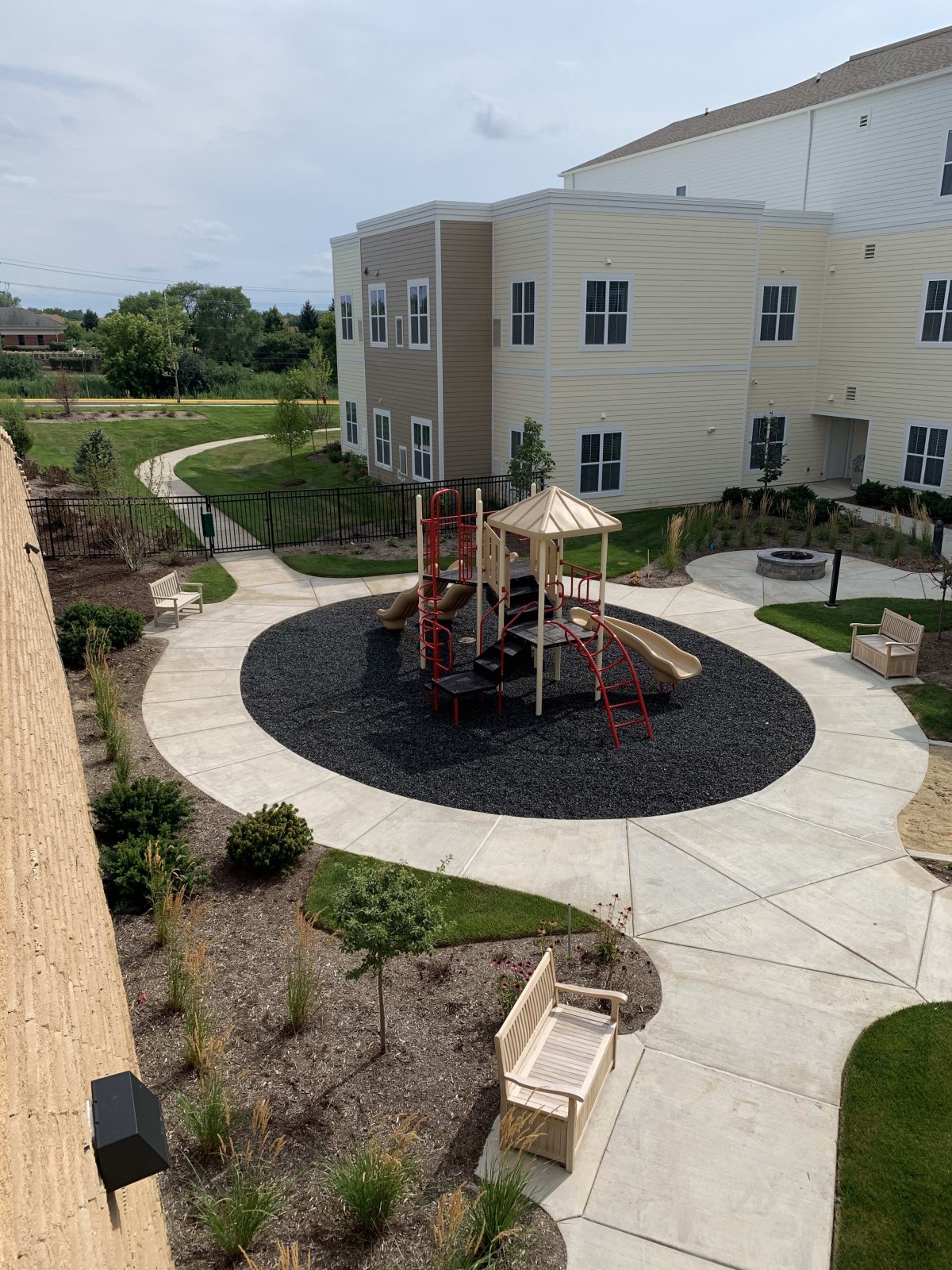 A small playground with a slide located in an apartment complex courtyard, surrounded by landscaped paths.