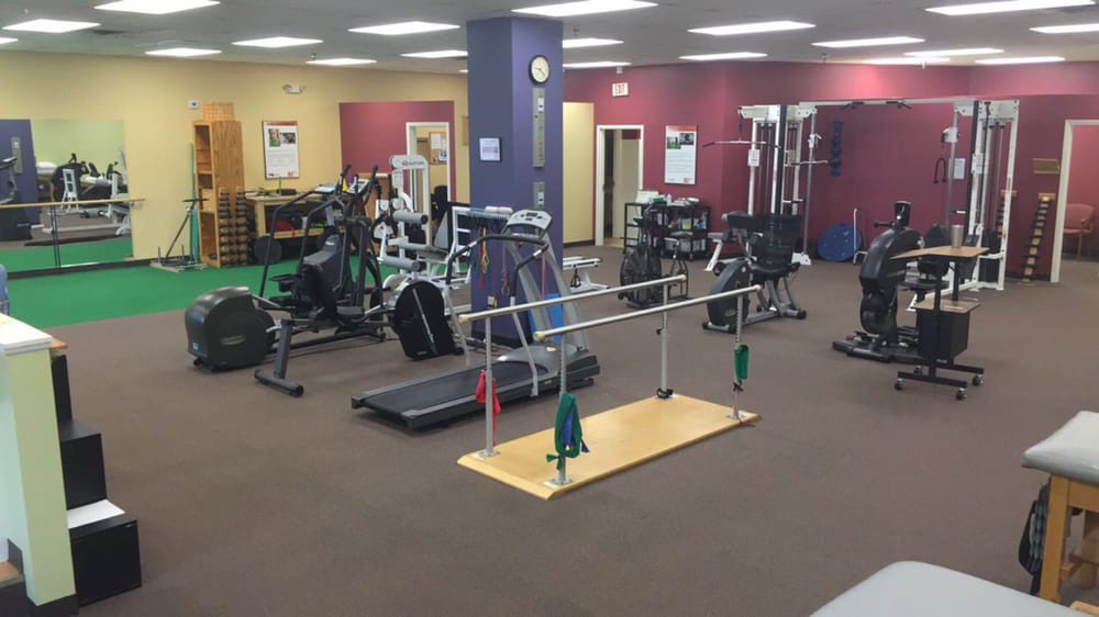 A spacious gym with various exercise equipment including treadmills, weights, and parallel bars.