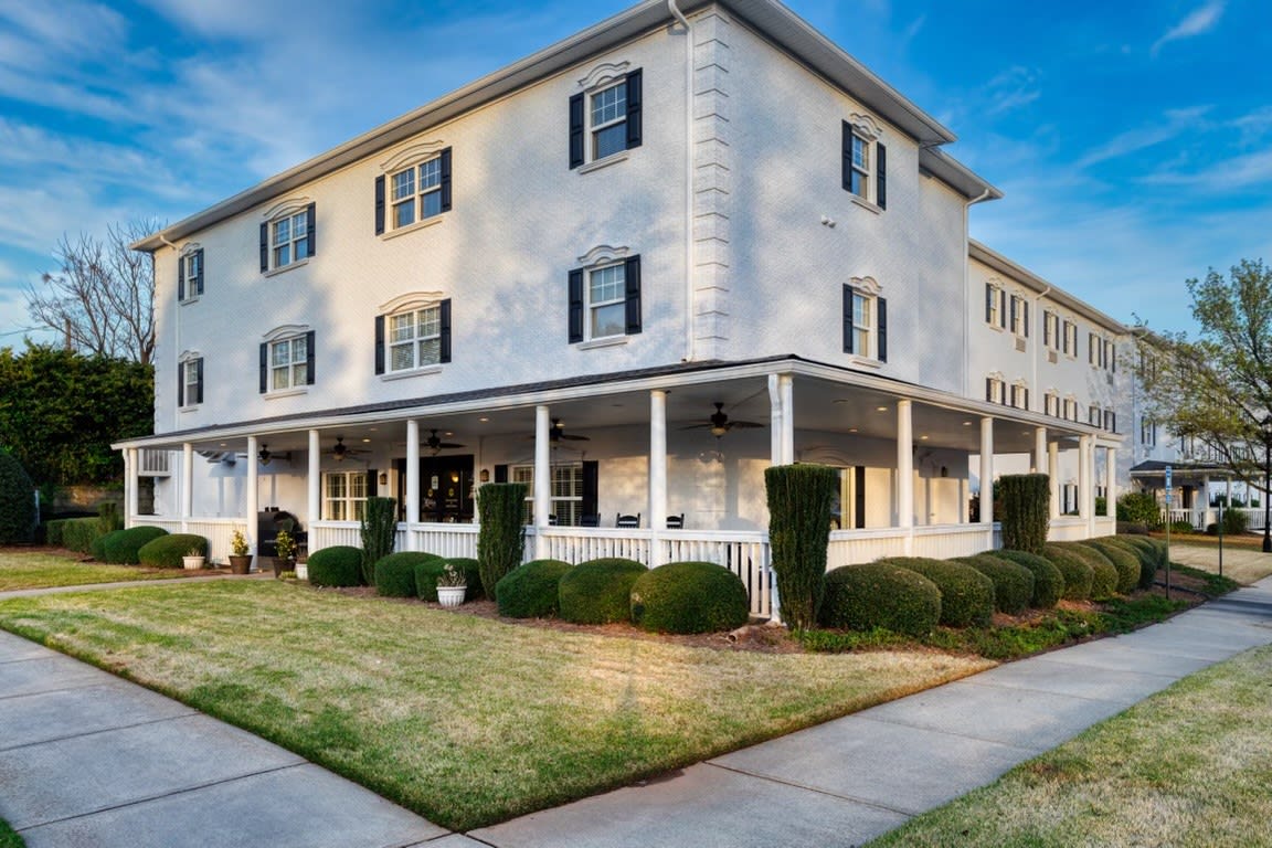 A large, three-story residential building with a wraparound porch and neatly trimmed lawn.