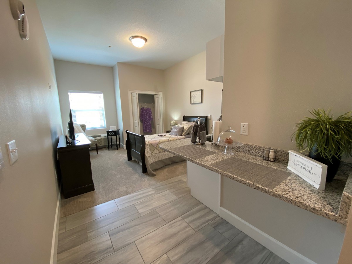 A cozy studio apartment featuring a small kitchenette and a comfortable sleeping area, illuminated by natural light.
