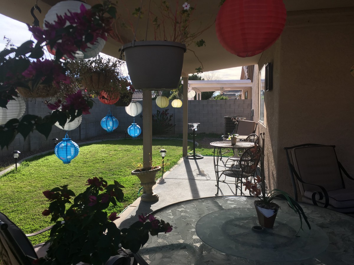 A sunny patio adorned with colorful lanterns, outdoor furniture, and lush plants.