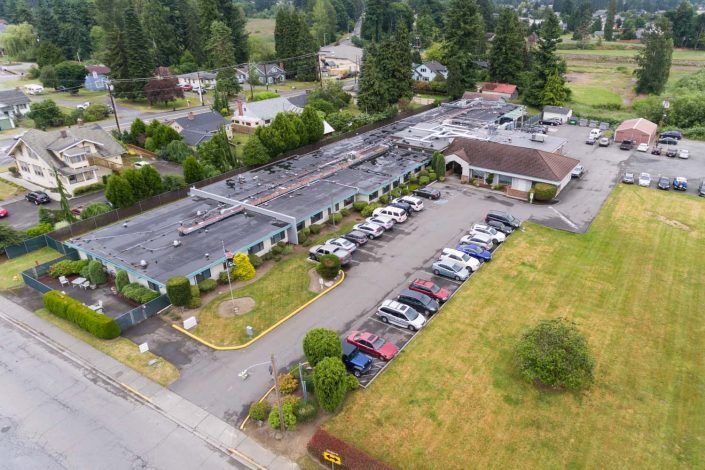 Aerial view of a building with an adjacent parking lot in a suburban area surrounded by trees.