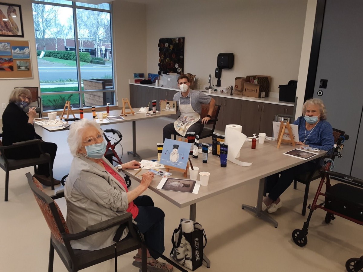 A group of senior citizens participating in an art class, painting while wearing masks and using various art supplies.
