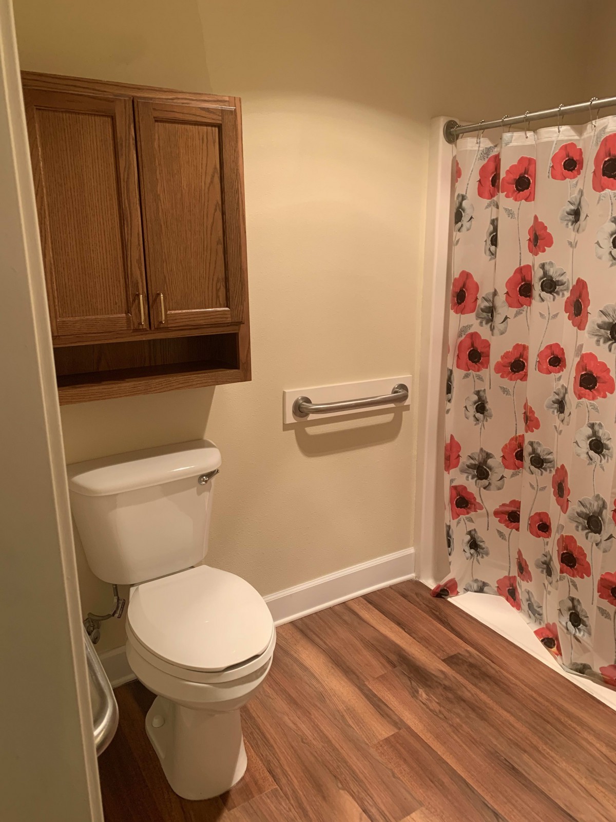 A cozy bathroom featuring a toilet, floral shower curtain, and wooden cabinetry.