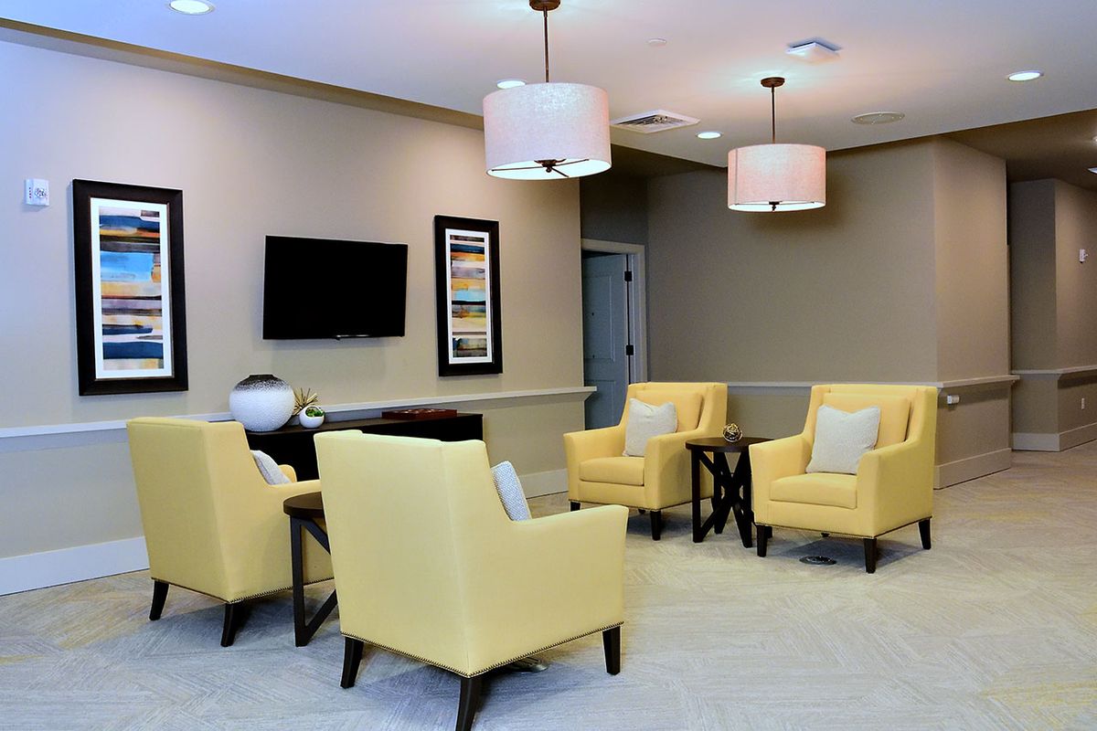 A modern living room featuring yellow chairs, a television, and elegant lighting.