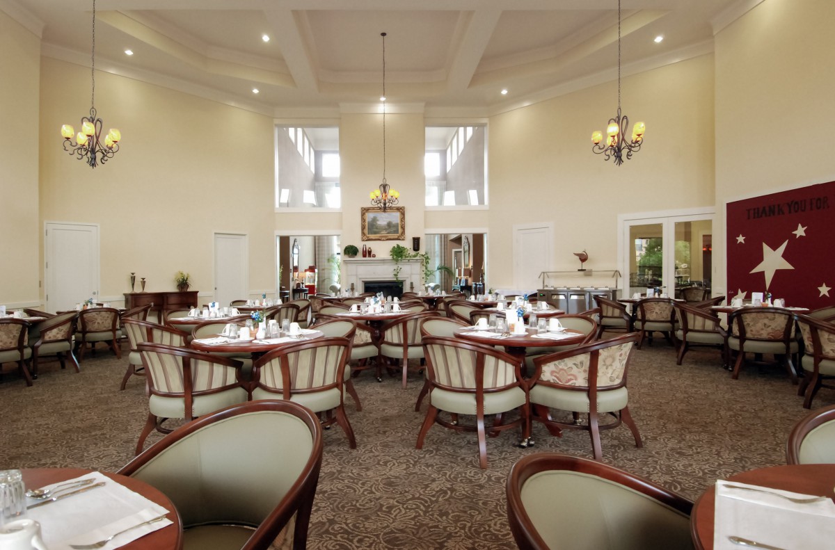 A spacious dining area with elegant tables and chairs, a chandelier, and large windows.