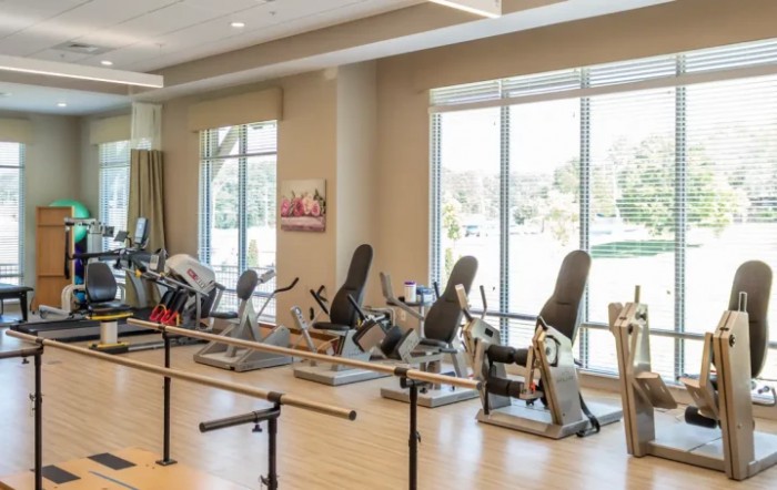 A physical therapy room with various exercise equipment and large windows.