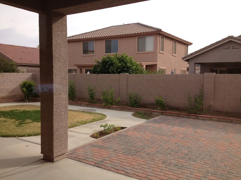 A suburban backyard with a paved area, lawn, and surrounding fence.