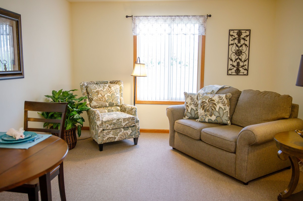 A cozy living room with a beige couch, floral armchair, and natural light from a window.