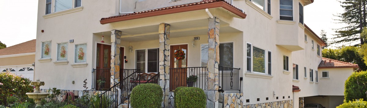 A cozy front porch with stone columns and a wooden door decorated with a wreath.