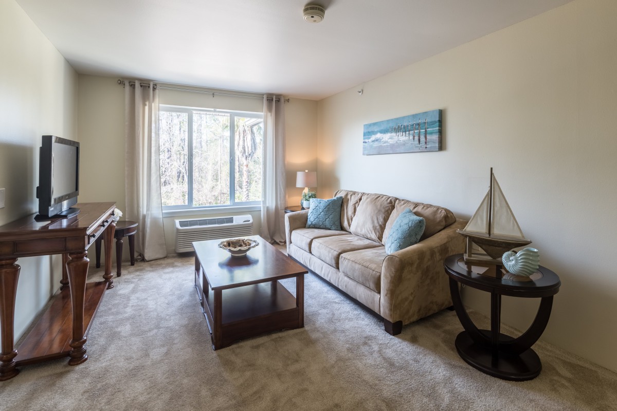 A cozy living room with a sofa, coffee table, and large window offering natural light.