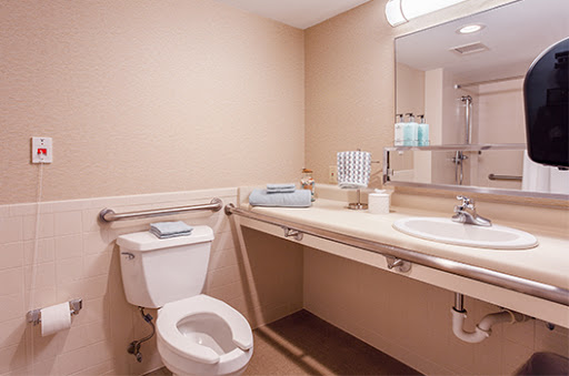 A clean and accessible bathroom featuring a toilet, sink, and safety handrails.