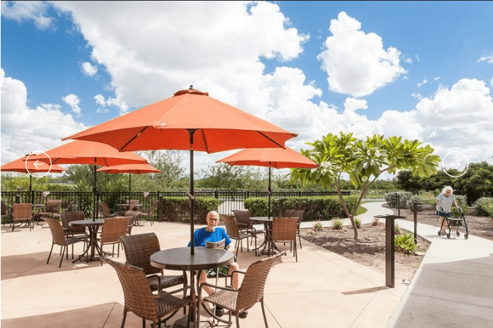 A sunny outdoor patio with tables, chairs, and orange umbrellas under a clear blue sky.
