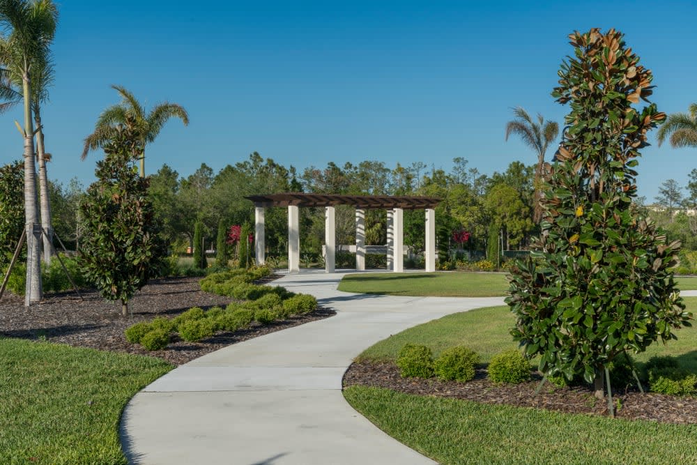 A scenic garden pathway lined with trees and leading to a structure with columns.