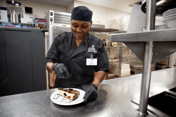 A chef garnishes a dessert plate in a professional kitchen.