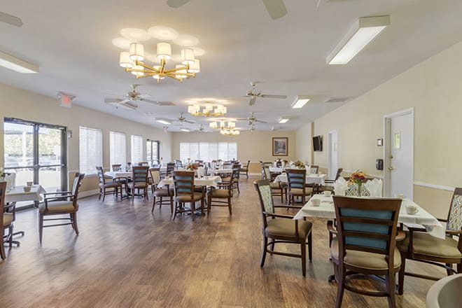 A spacious dining room with neatly arranged tables and chairs, featuring large windows and elegant chandeliers.