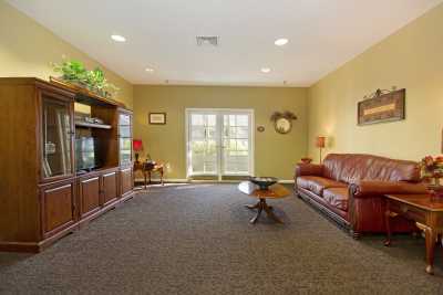 A spacious living room with a brown leather sofa, a coffee table, and an entertainment center, featuring large windows and warm lighting.