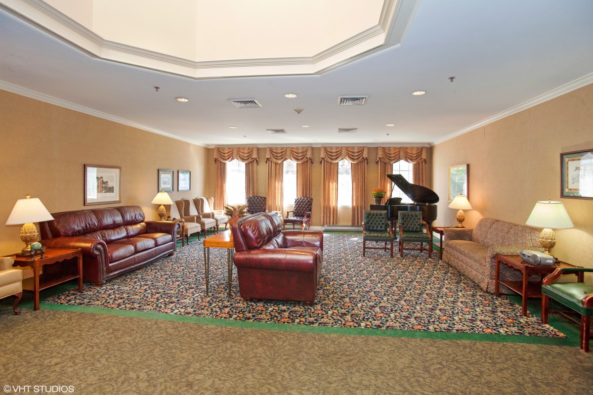A spacious lounge area featuring leather sofas, a grand piano, and ample natural light from large windows.