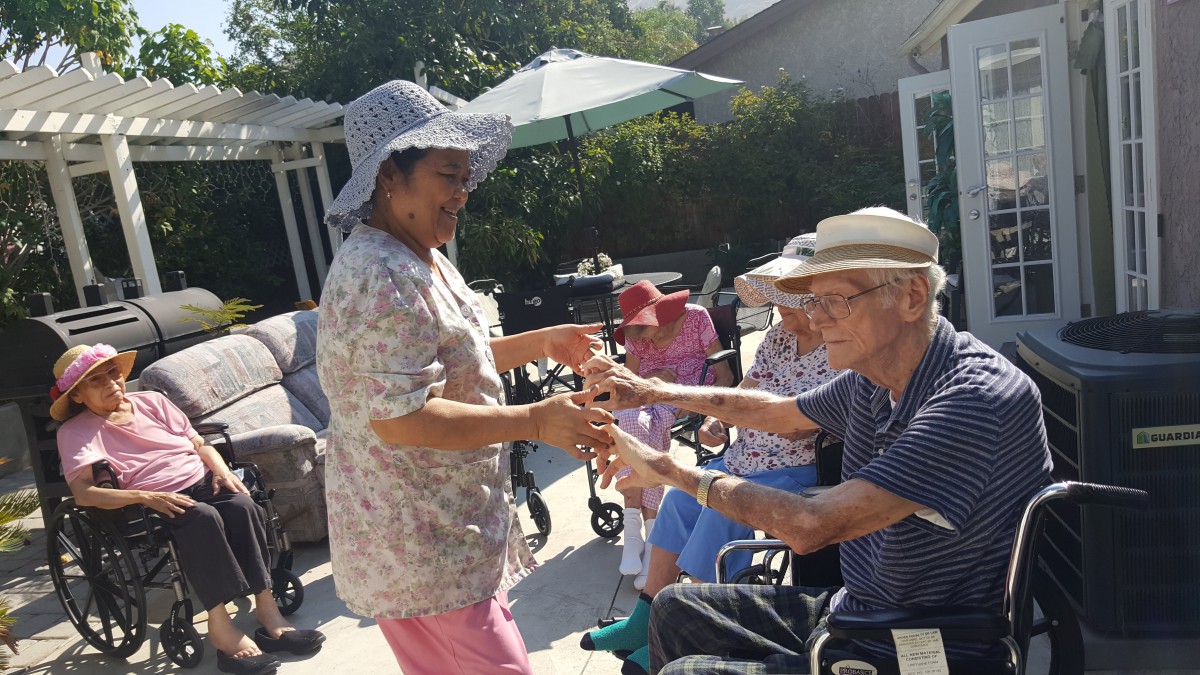 A group of elderly people enjoying a sunny day outdoors, with two individuals dancing together.